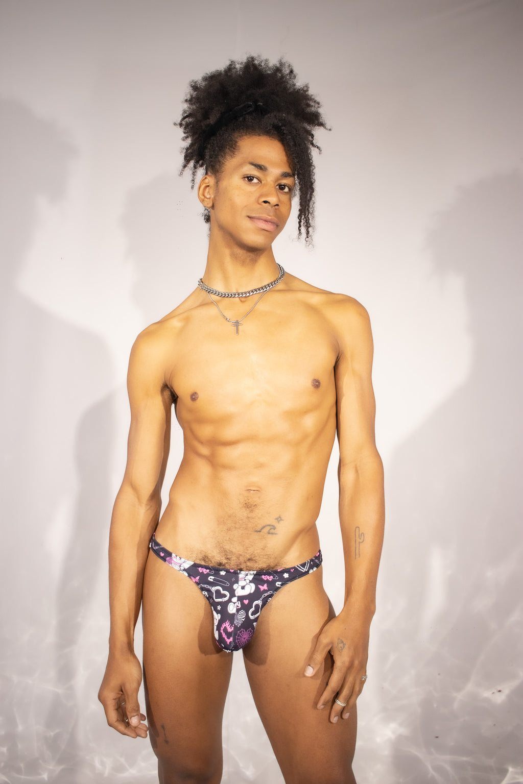 Person wearing a black thong with pink and white patterns against a plain background