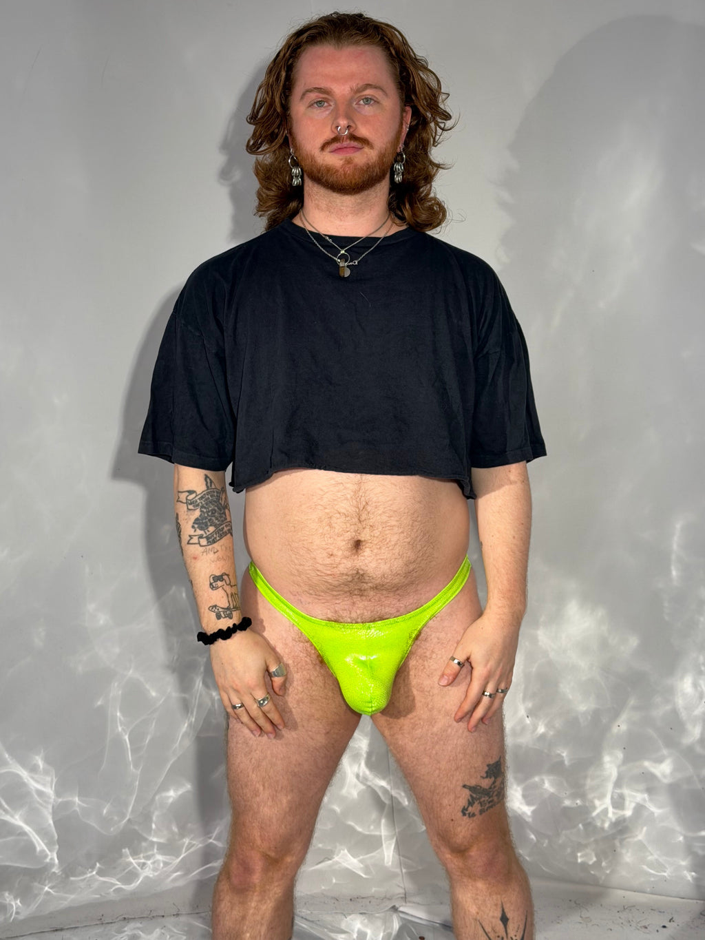Person wearing a black t-shirt and neon green thong on a reflective surface.