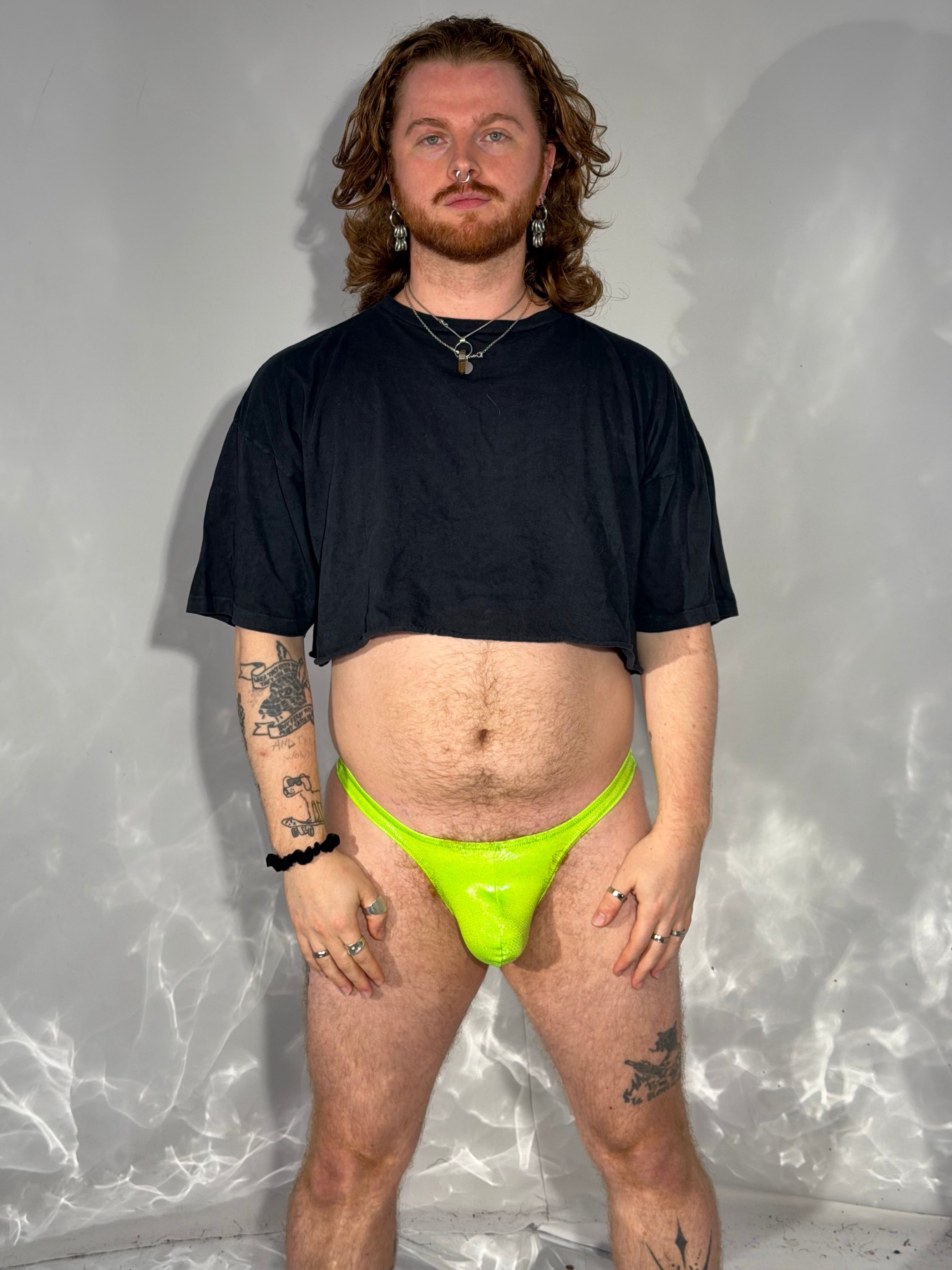 Person wearing a black t-shirt and neon green thong on a reflective surface.