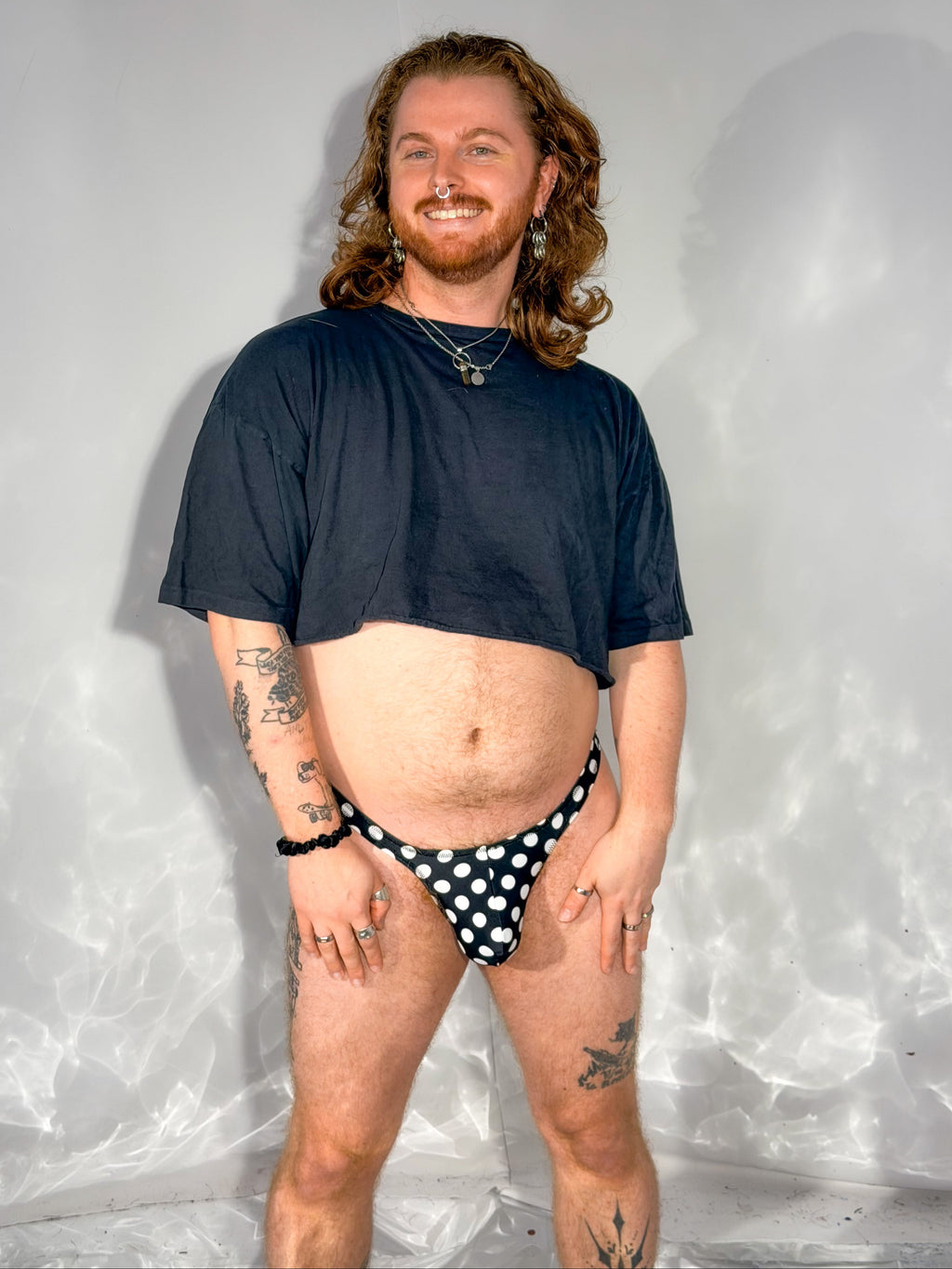 Person wearing a black t-shirt and polka dot underwear against a textured white background