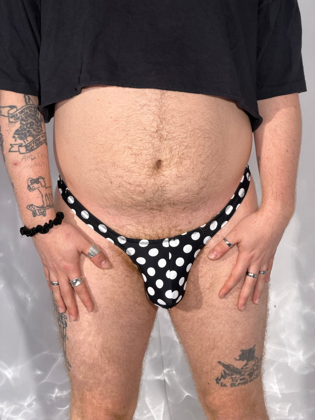 Person wearing a black polka dot thong against a neutral background