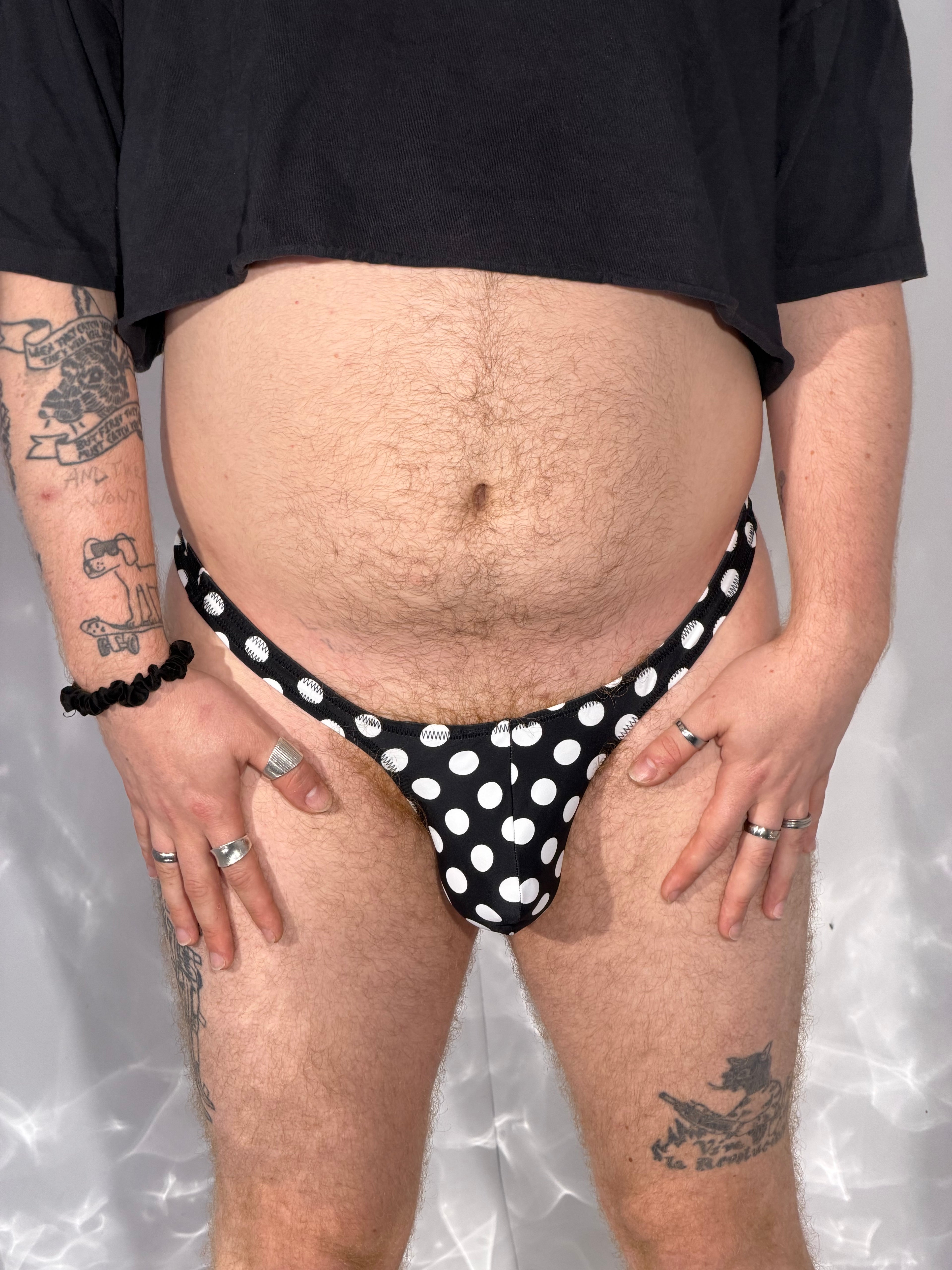 Person wearing a black polka dot thong against a neutral background