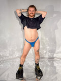 Person wearing a black shirt and blue underwear standing in a room with white walls and a reflective floor.
