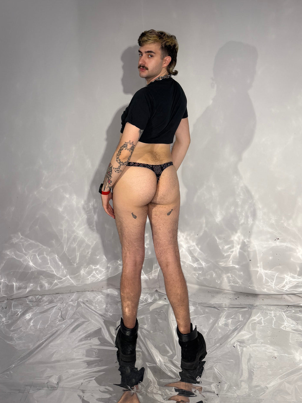 Person wearing a black top and underwear in a room with white walls and a plastic sheet.