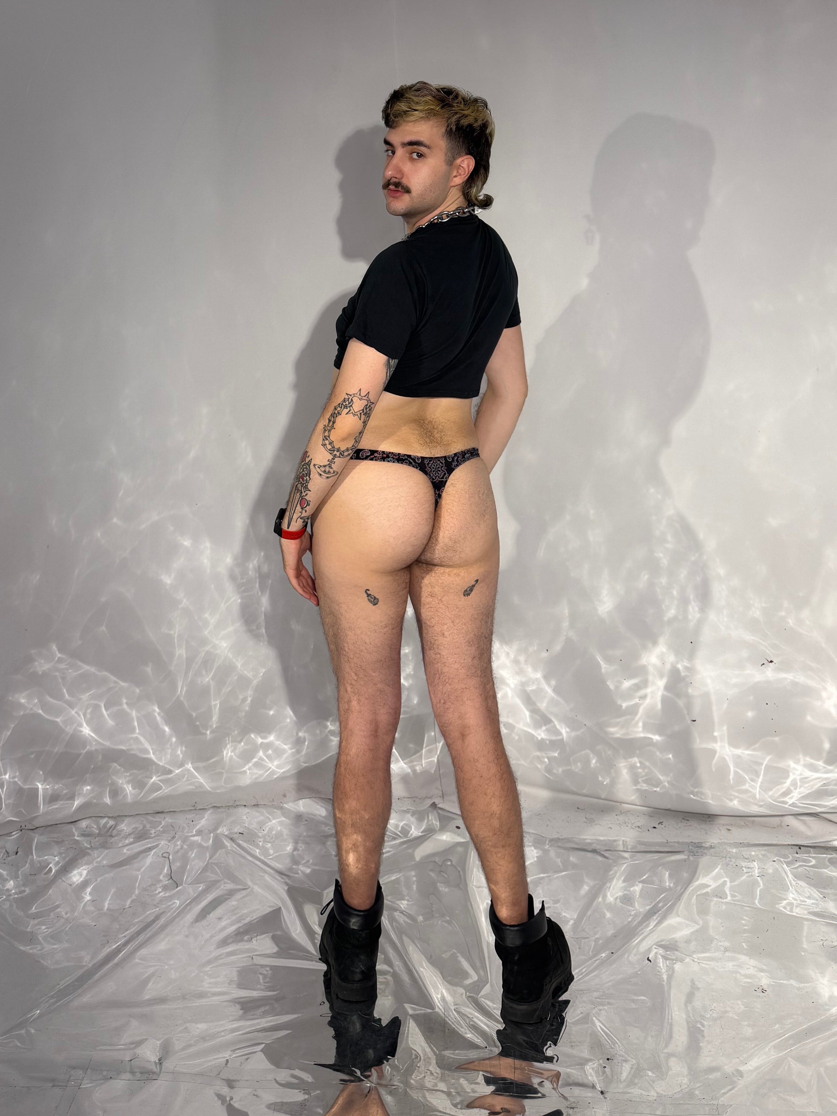 Person wearing a black top and underwear in a room with white walls and a plastic sheet.