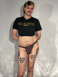 Person wearing a black t-shirt with text and patterned underwear on a plain background