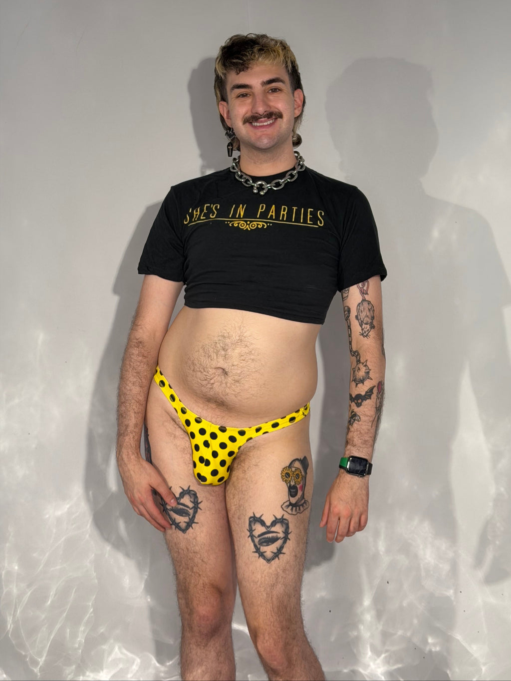 Person wearing a black t-shirt and yellow polka dot thong on a reflective surface