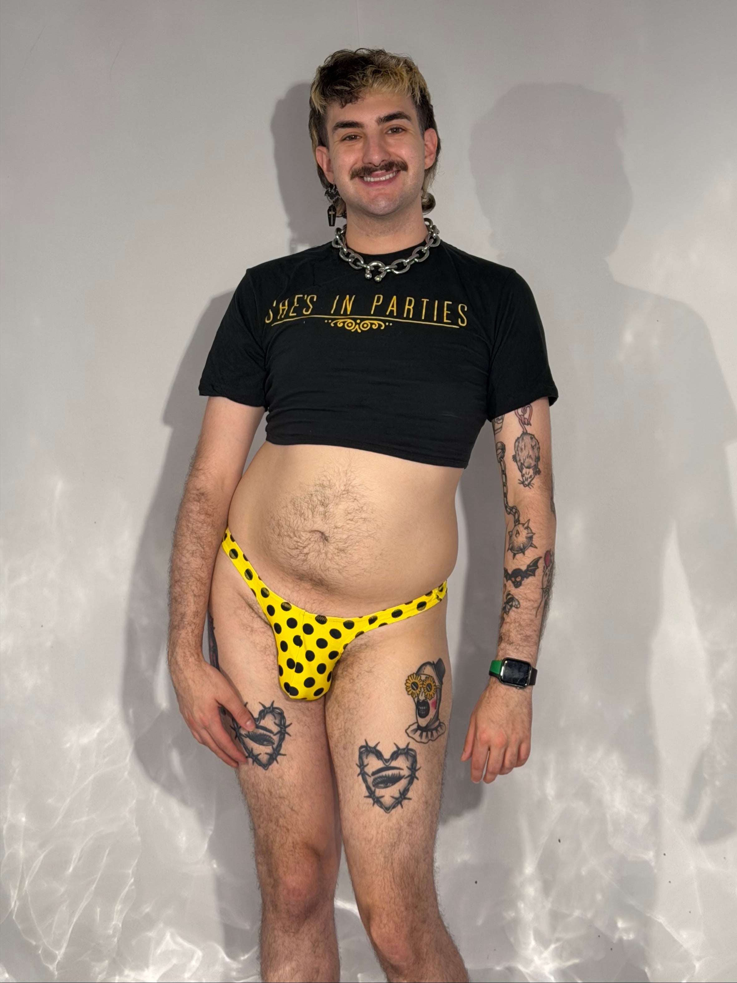 Person wearing a black t-shirt and yellow polka dot thong on a reflective surface