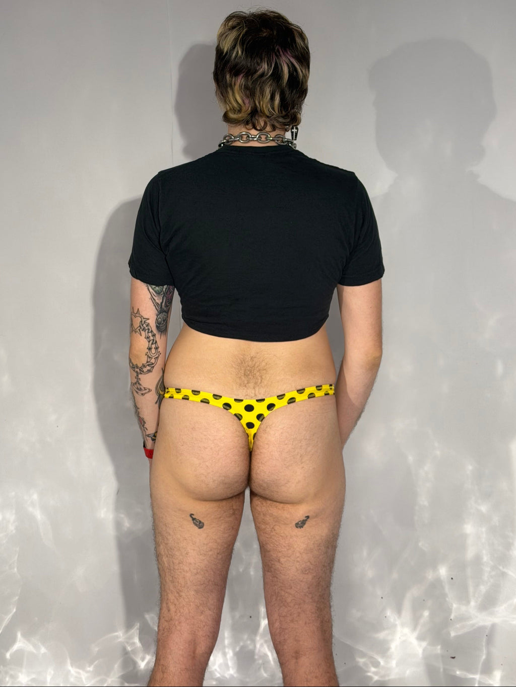 Person wearing a black top and yellow thong on a reflective surface