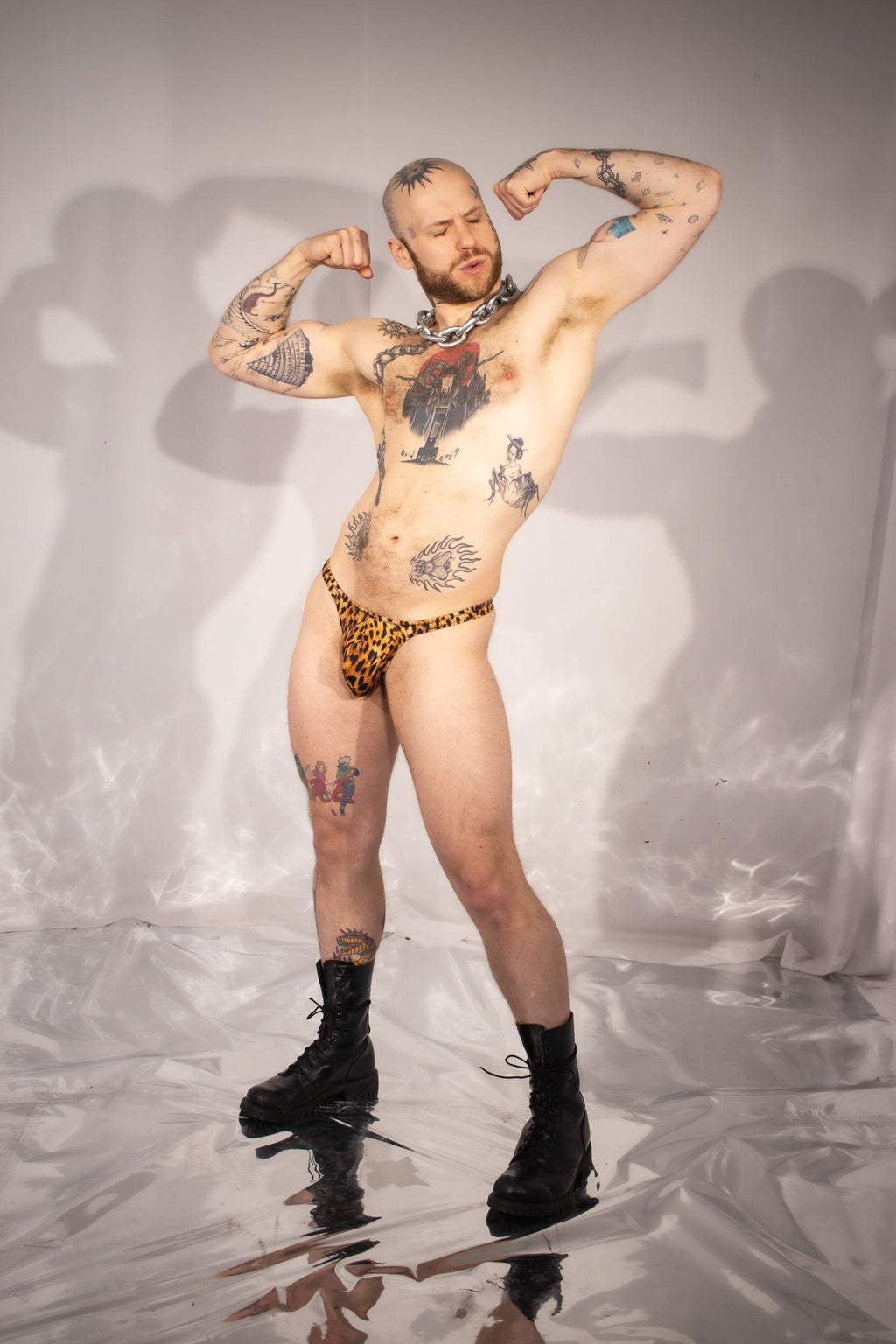Man with tattoos wearing leopard print underwear on a reflective surface