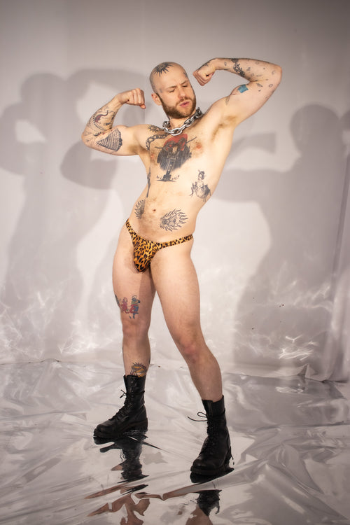 Man with tattoos wearing leopard print underwear on a reflective surface