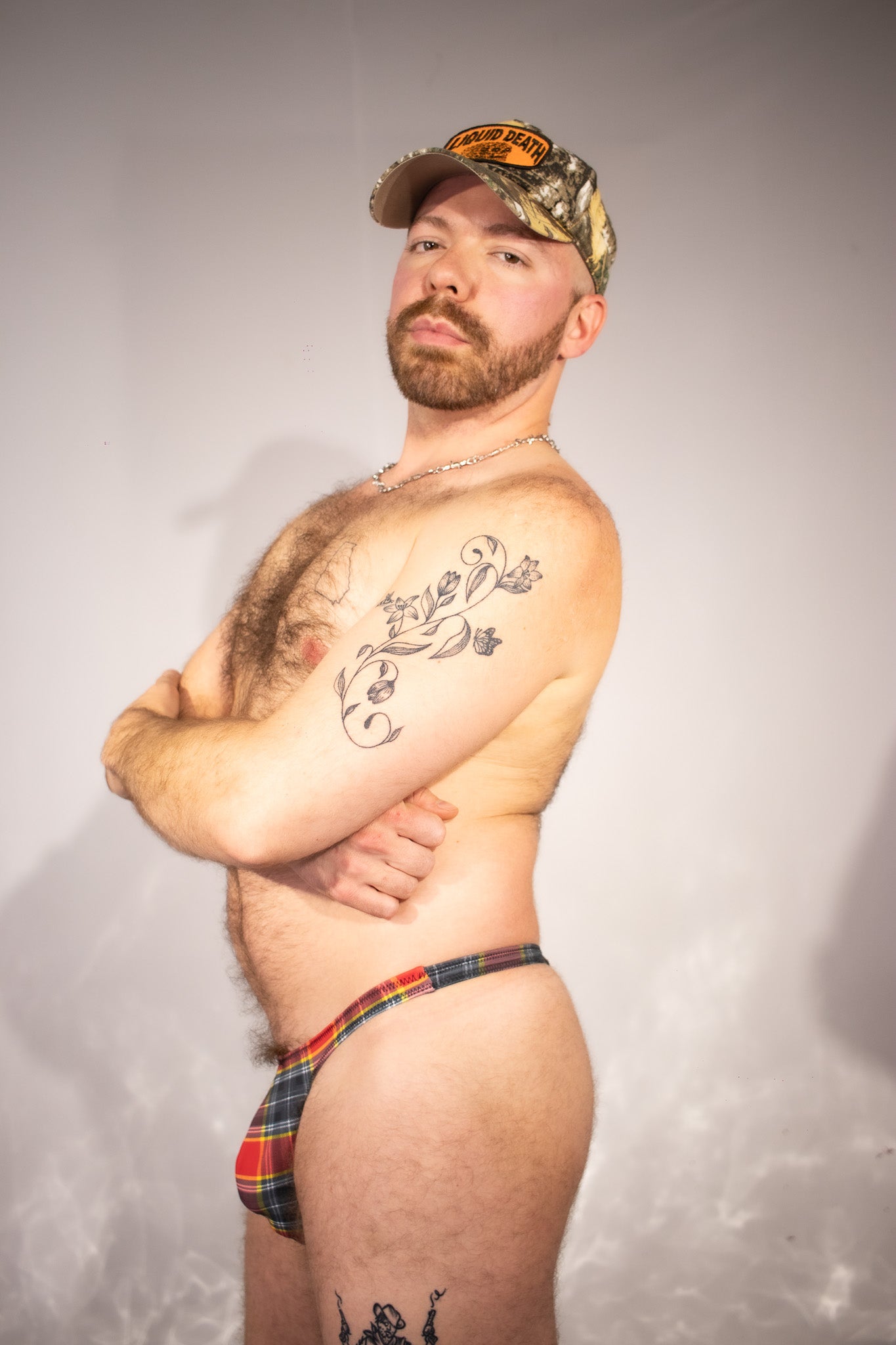 Man wearing a camouflage cap and a plaid thong against a plain background