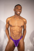 Man wearing a purple patterned velvet thong against a plain background